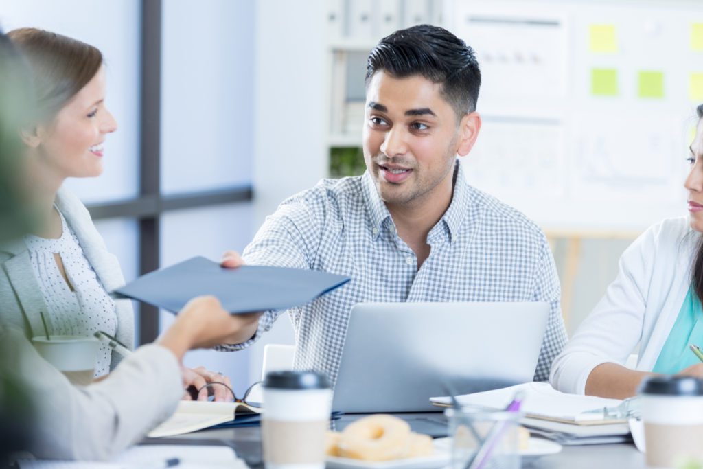 Office workers discussing around a table with man passing a folder